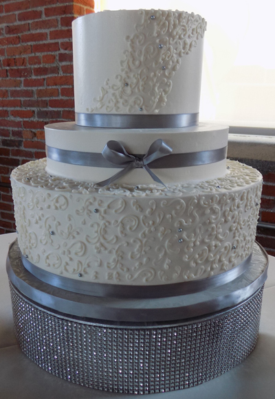 3 Tier buttercream wedding cake, decorated with small buttercream scrolls, silver sugar pearls/dragees, silver ribbons and placed on a bling/diamond wedding cake stand. Cake was delivered to John Wright Restaurant in Wrightsville PA