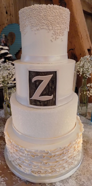 Four tier buttercream wedding cake decorated with sugar pearls, sugar crystals, fondant frills and ribbons, as well as a wooden fondant frame with initial of bride and groom's last name. Cake was delivered at the Ironstone Ranch in Elizabethtown PA